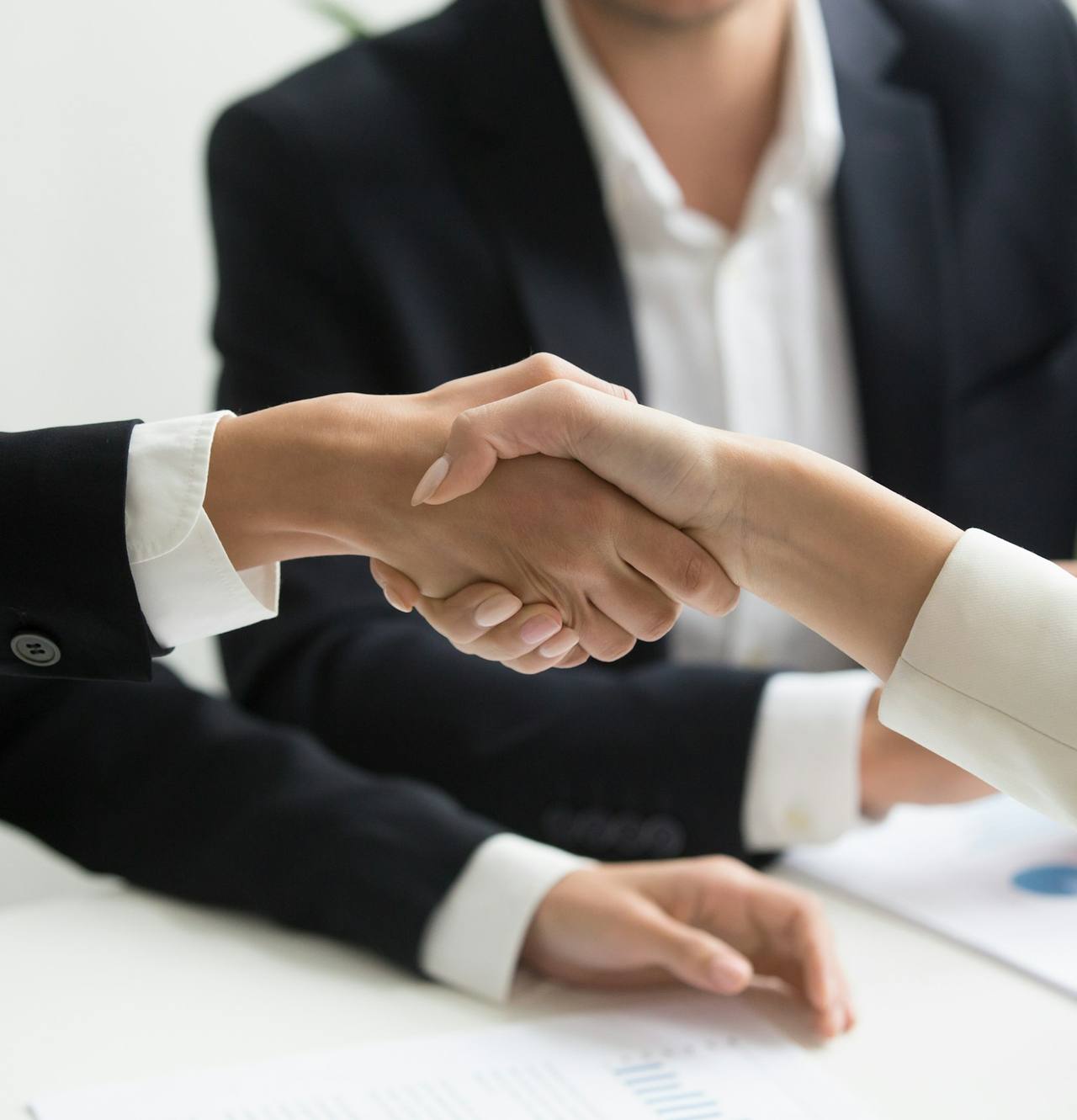 Deux professionnels se serrent la main au-dessus d'une table de travail, documents et graphiques devant eux.
