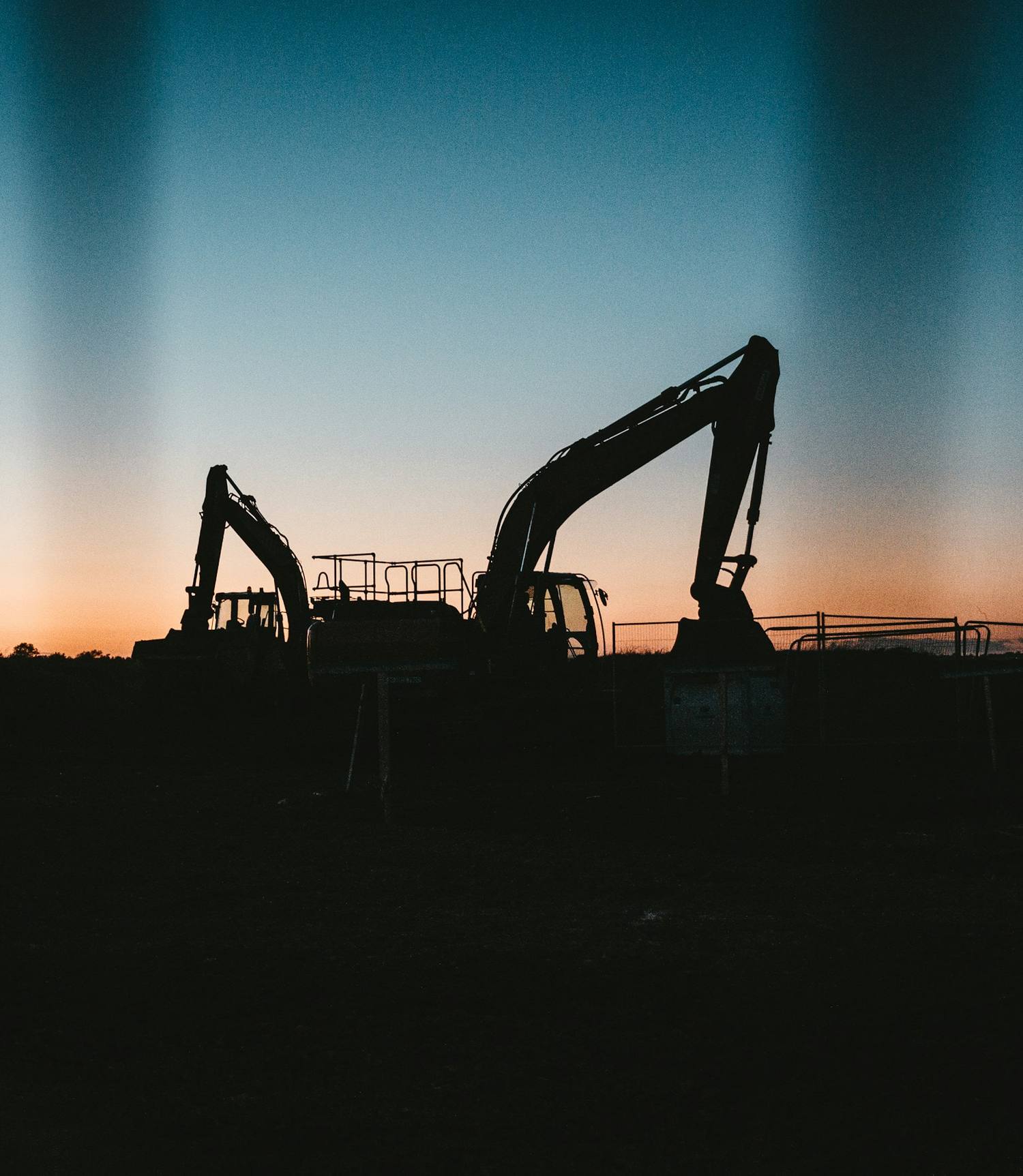 Deux pelles hydrauliques en silhouette sur un chantier au coucher du soleil.