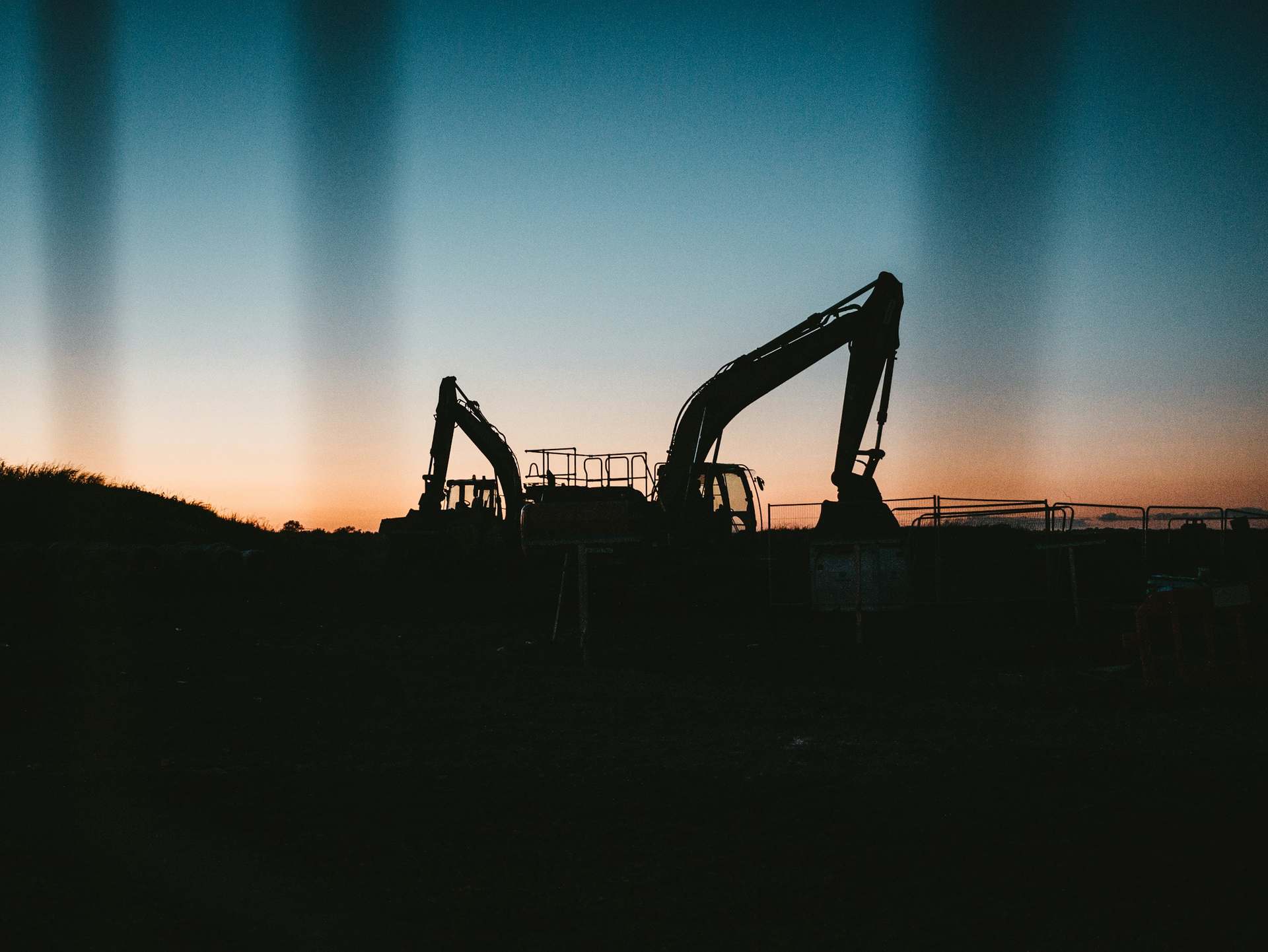 Deux pelles hydrauliques en silhouette sur un chantier au coucher du soleil.