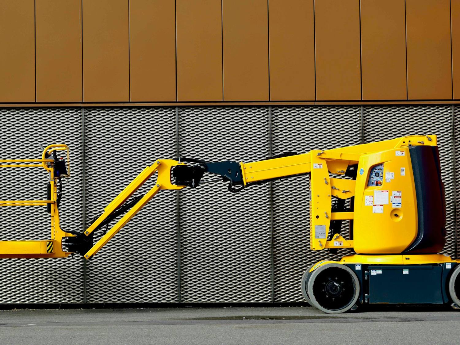 Nacelle articulée jaune devant une façade métallique perforée.