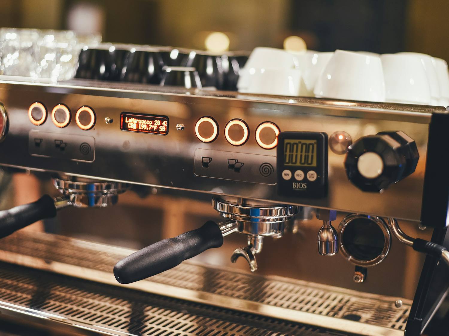 Façade d'une machine à espresso professionnelle en inox, tasses posées dessus.