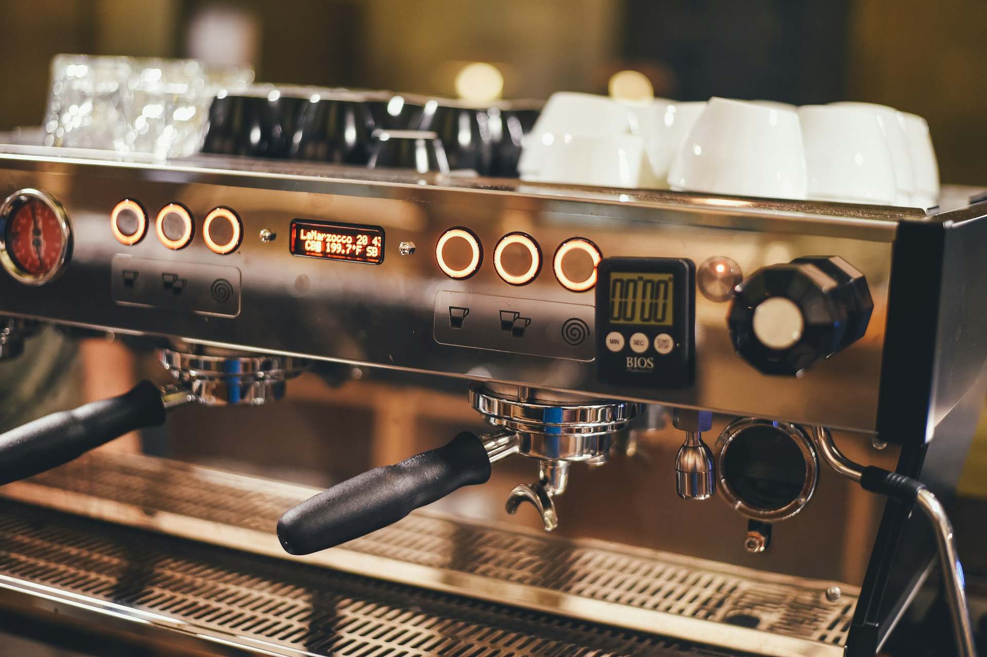 Façade d'une machine à espresso professionnelle en inox, tasses posées dessus.