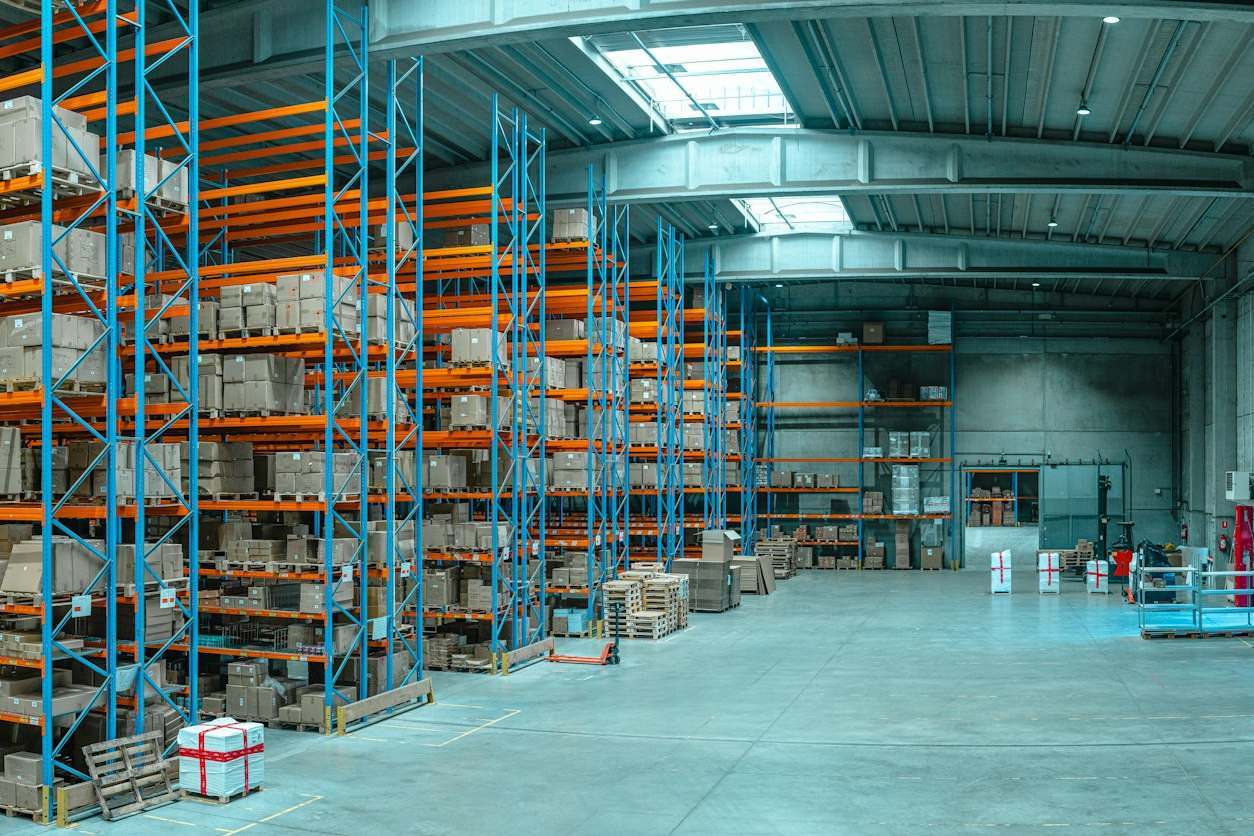 Entrepôt avec de hautes étagères métalliques bleues remplies de cartons.