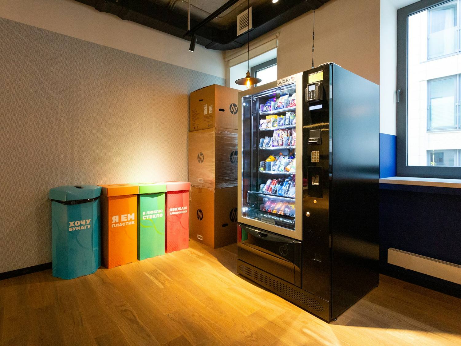Distributeur automatique noir dans un espace de pause lumineux, à côté de bacs de tri.