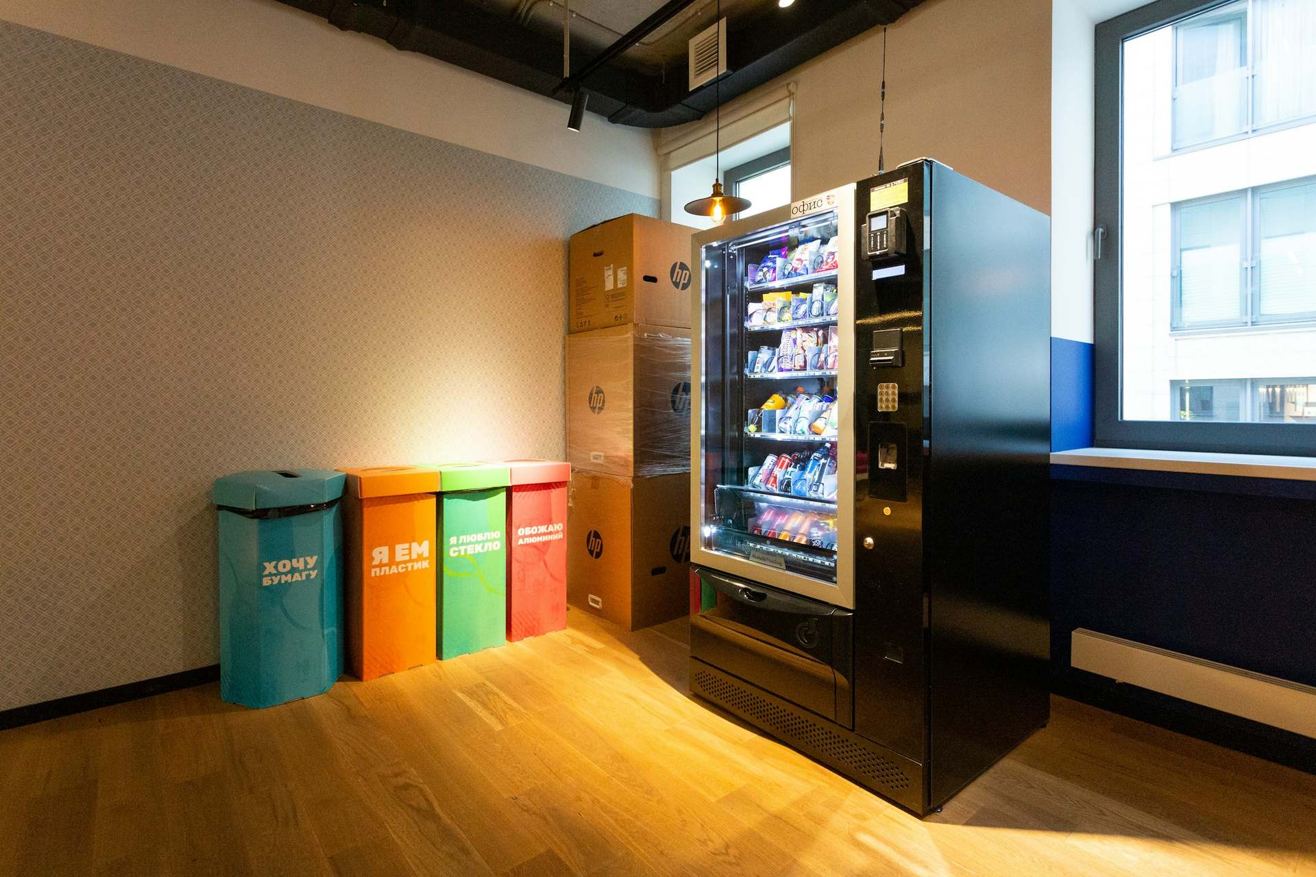 Distributeur automatique noir dans un espace de pause lumineux, à côté de bacs de tri.